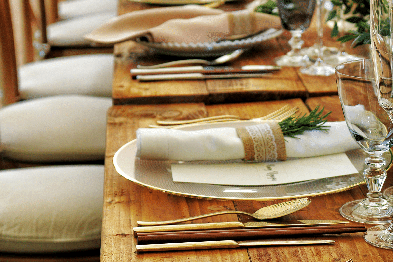 A long, elegantly set dining table stretches into the distance, featuring tables aranged with plates and napkins.