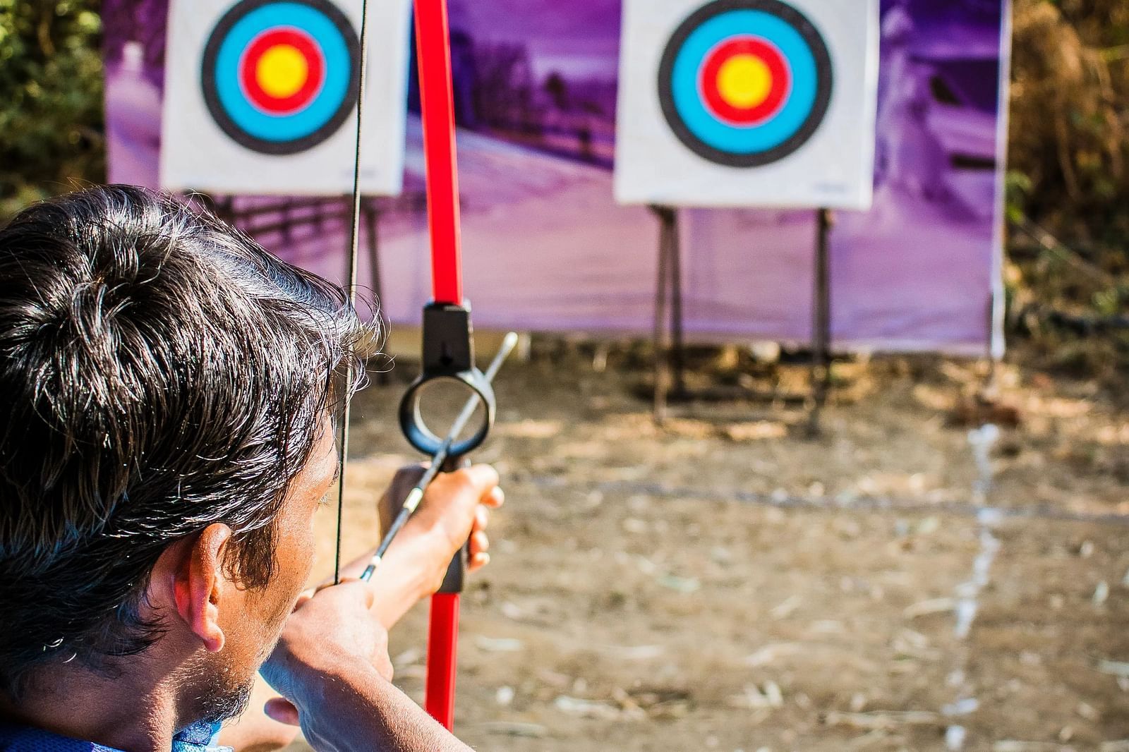 Person aiming an arrow at a target, outdoor activity, focus and concentration.