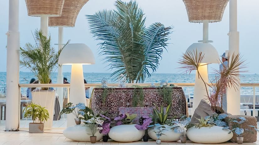 A luxurious outdoor lounge area at Living Room Beach Resort, Morjim, Goa featuring white planters holding lush green plants, illuminated by stylish lamps, all set against a backdrop of the ocean.