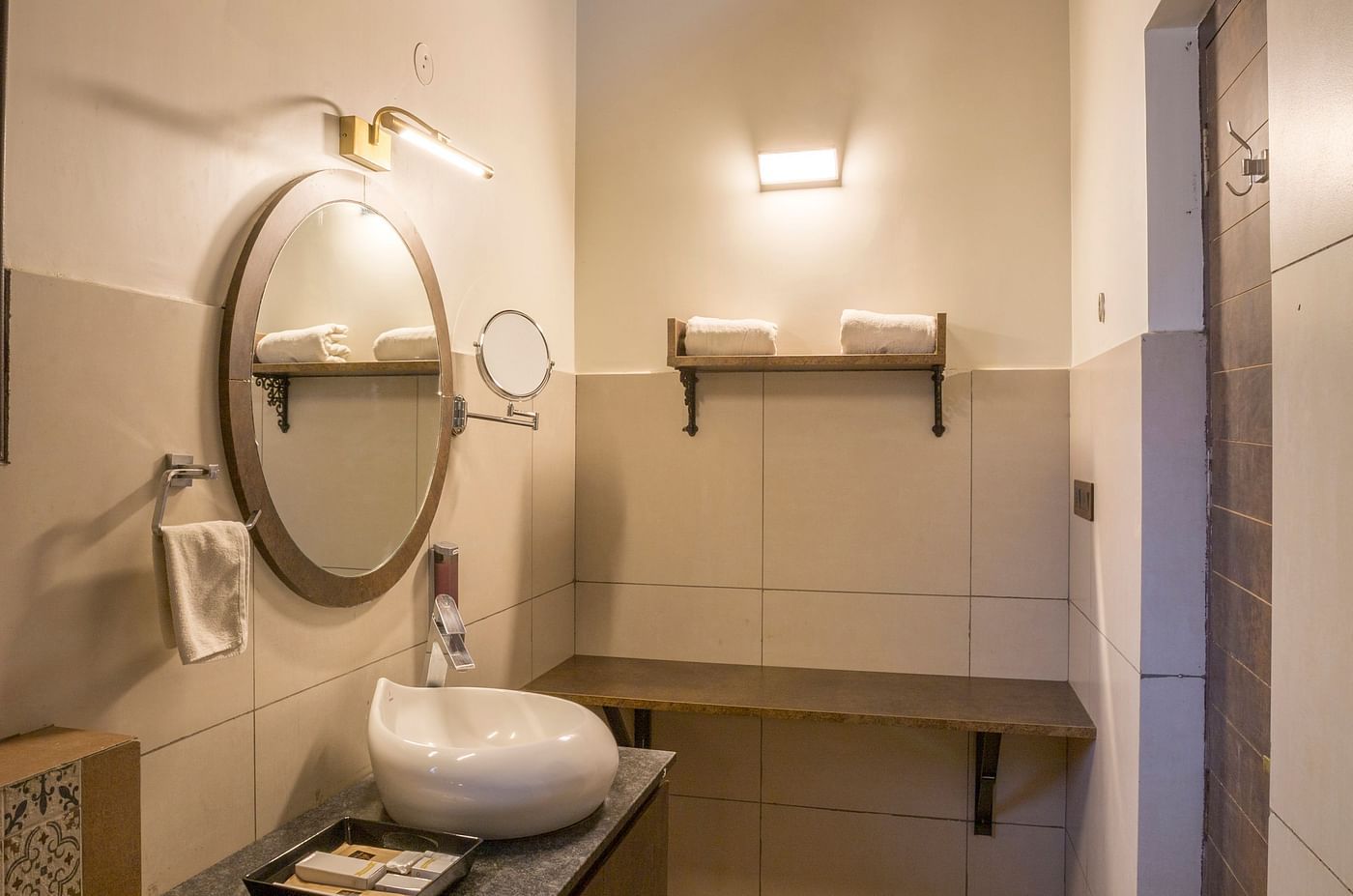 Bathroom with circular mirror and wooden vanity setup at Nirantara Resort