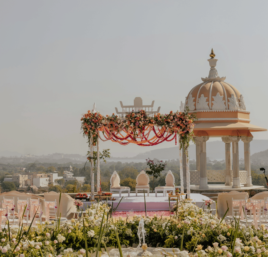 A wedding set up featuring a decorated canopy and a small architectural structural surrounded by plans and flowers.