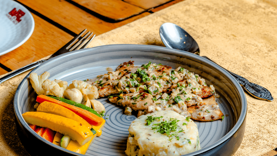 Grilled fish with rice and steamed vegetables at Marble Arch, located within Noor-Us-Sabah Palace, Bhopal, served on a set table with a lit candle.