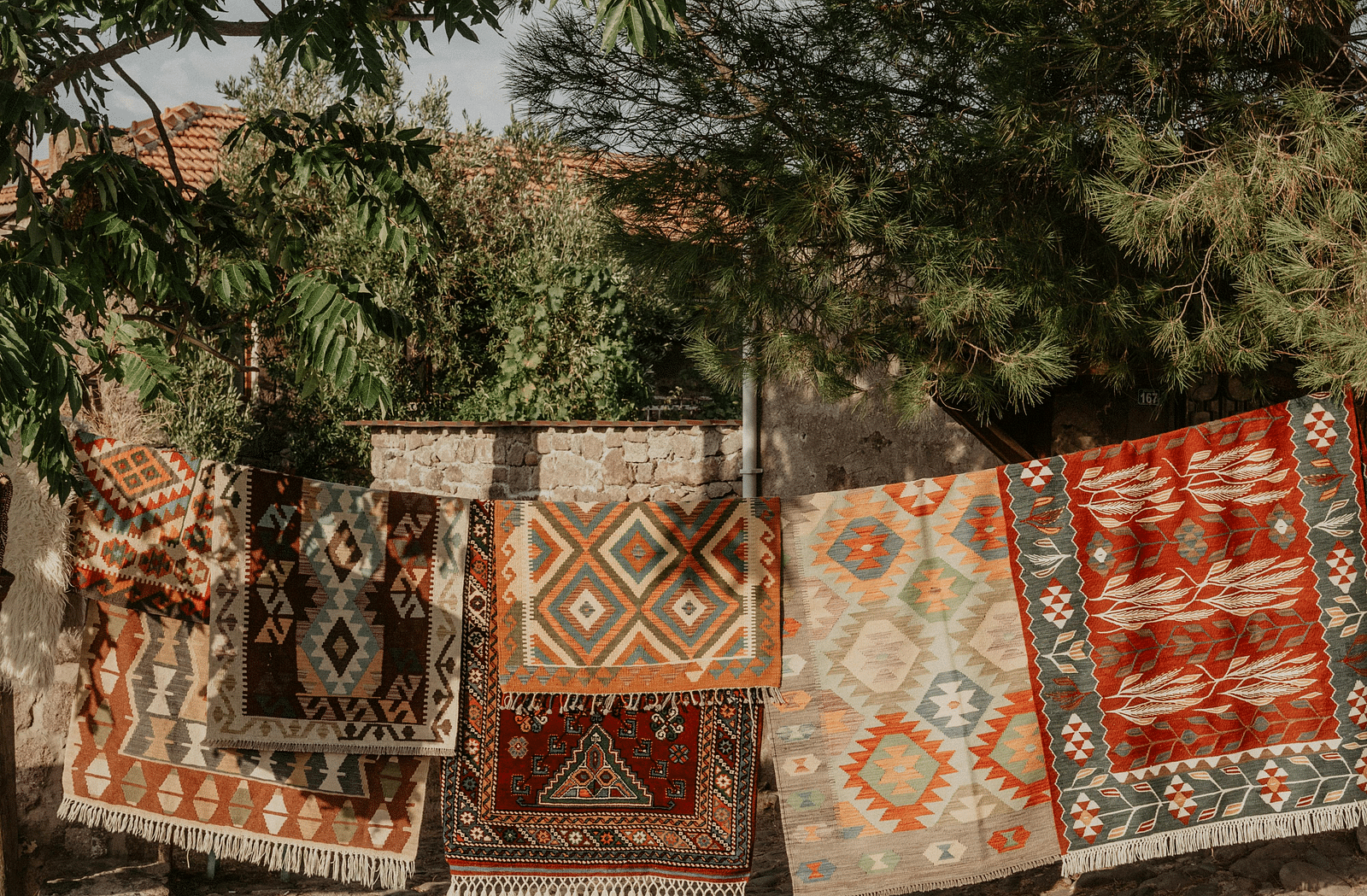 image of several carpets hanging on a string with trees shadowing them from above