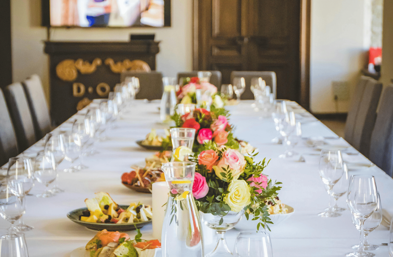 A long dining table decorated with flowers in the middle along with shiny glassware and cutlery set on the table.