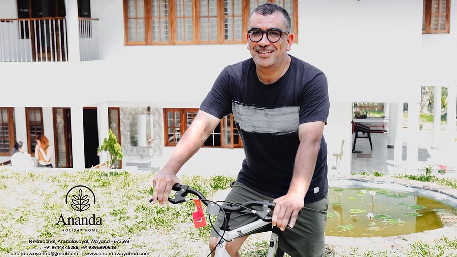 A man sitting on a bicycle standing in front of the facade of Ananda Holiday Home, Wayanad