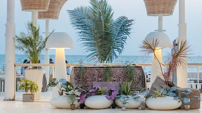 A luxurious outdoor lounge area at Living Room Beach Resort, Morjim, Goa featuring white planters holding lush green plants, illuminated by stylish lamps, all set against a backdrop of the ocean.