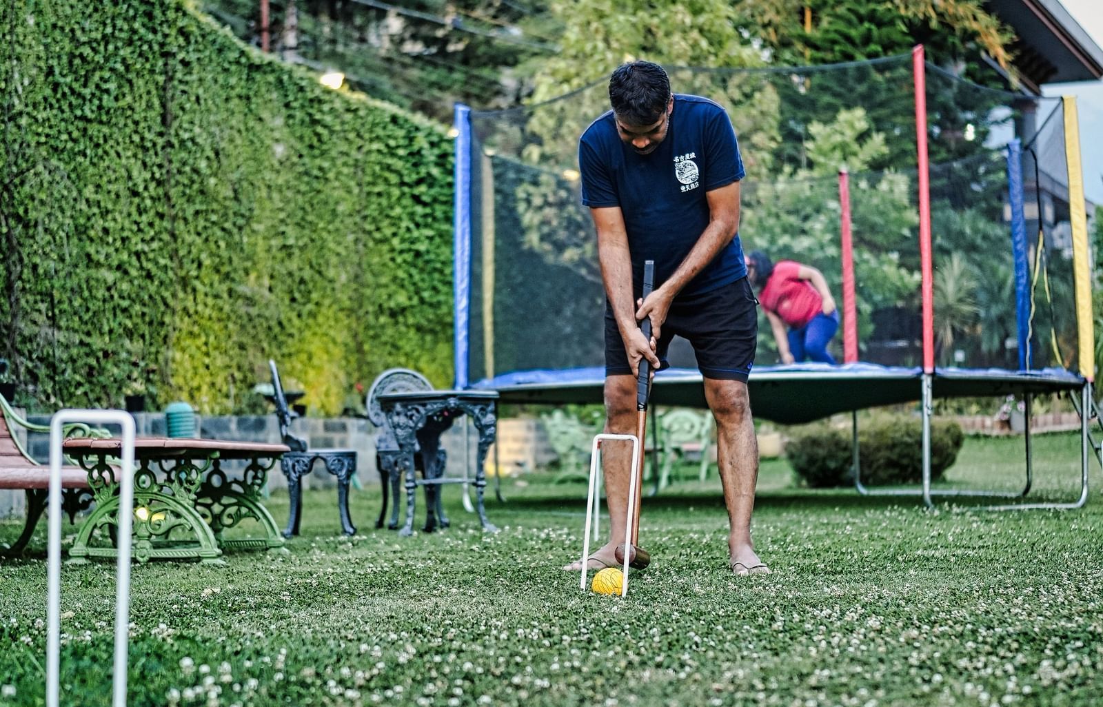 image of a man standing in-front of a trampoline and playing with a ball and a club, captured in  day time