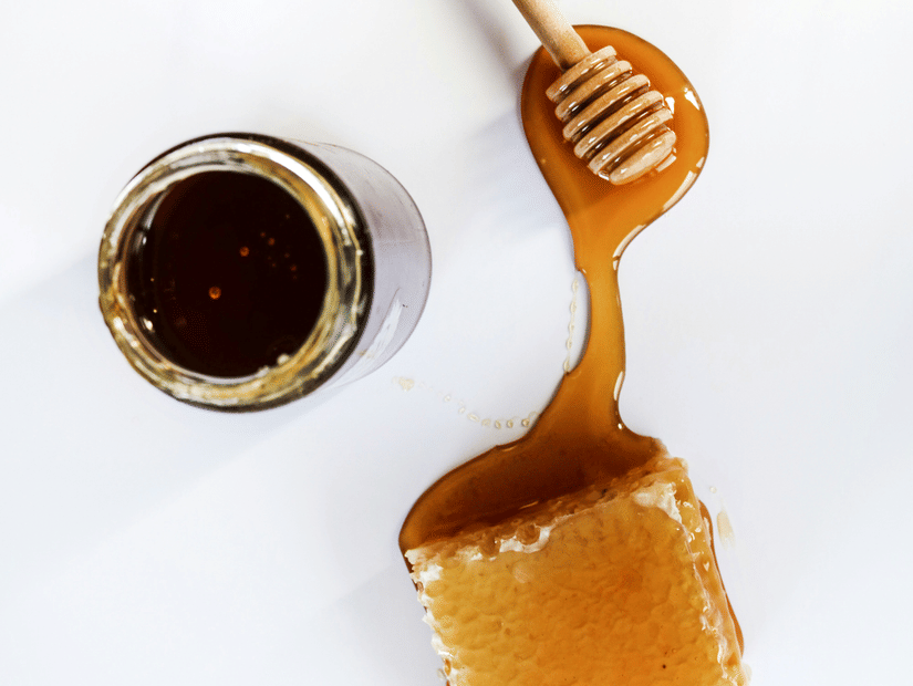 A top-down view of a ladle with honey flowing towards the honeycomb and a jar of honey next to it.