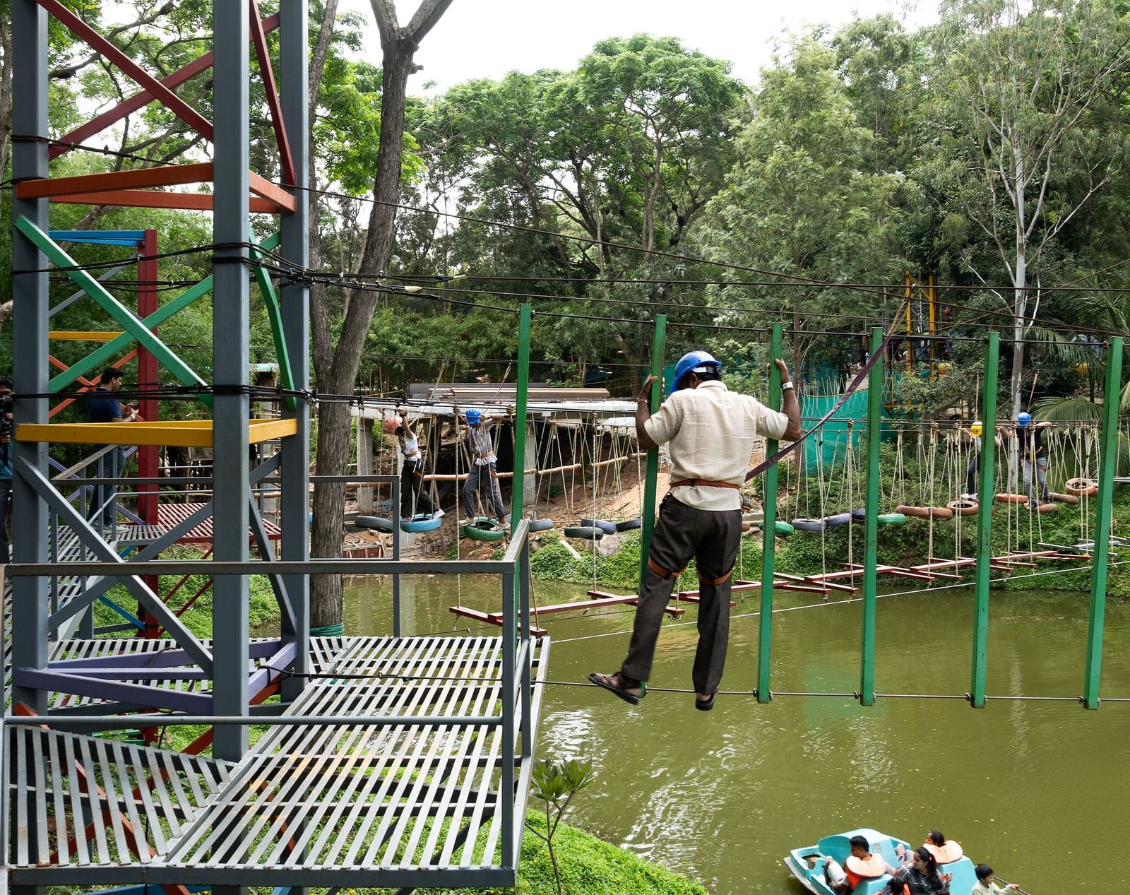 Two people are visible on an outdoor adventure course with ropes and wooden structures in a green environment | RD's Nature Retreat, Bangalore