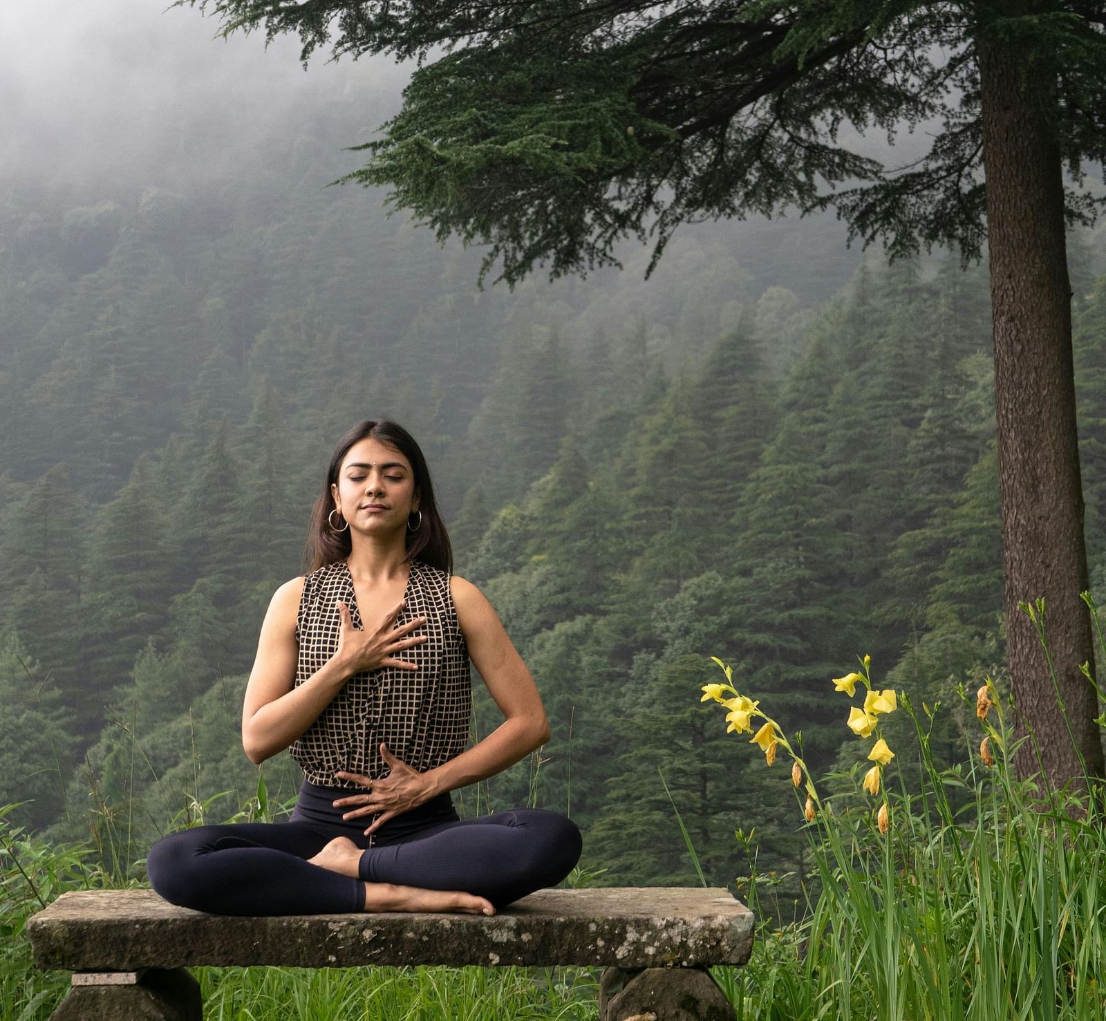 image of a woman doing meditation in the hilly area surrounded by lush greenery
