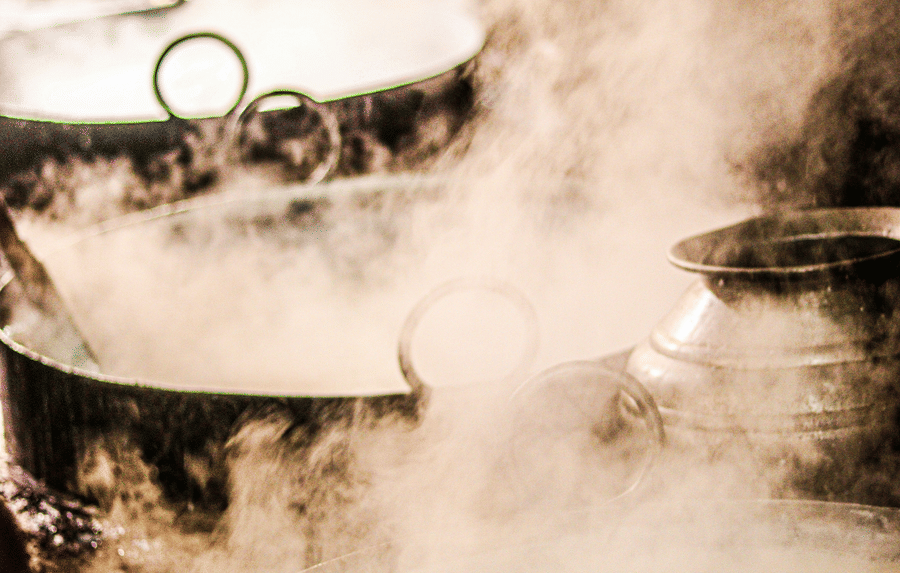 Metal pot cooking rice over a wood fire inside a rustic traditional kitchen.
