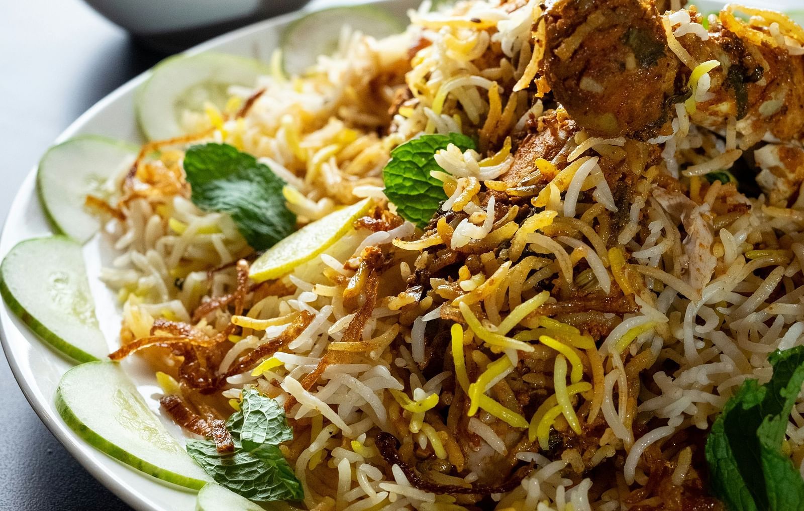 plate full of rice of various colors and meat topped with herbs with two small containers filled with an orange and white liquid respectively