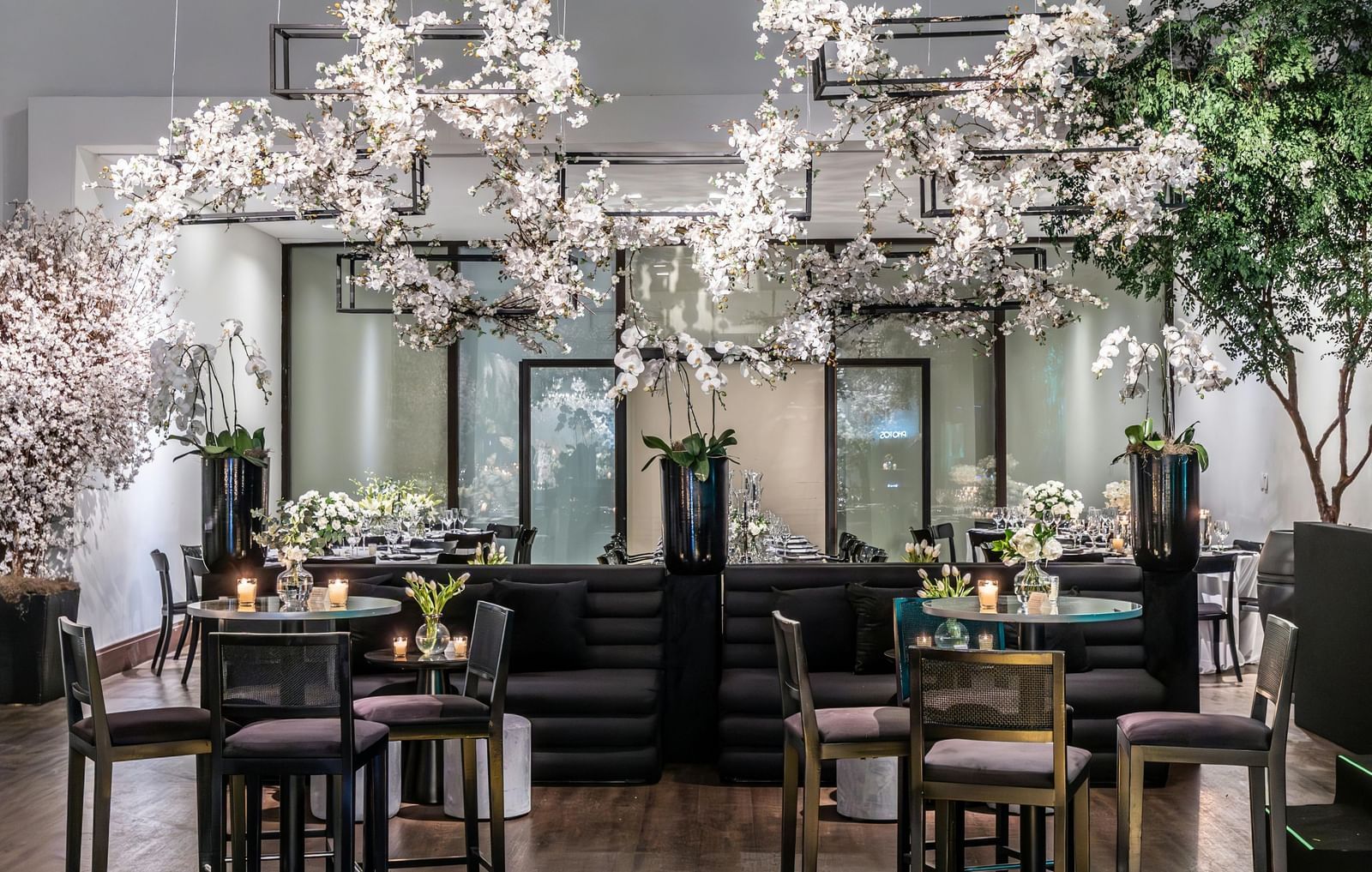 Brightly lit indoor event space with small tables, chairs, and floral decorations.