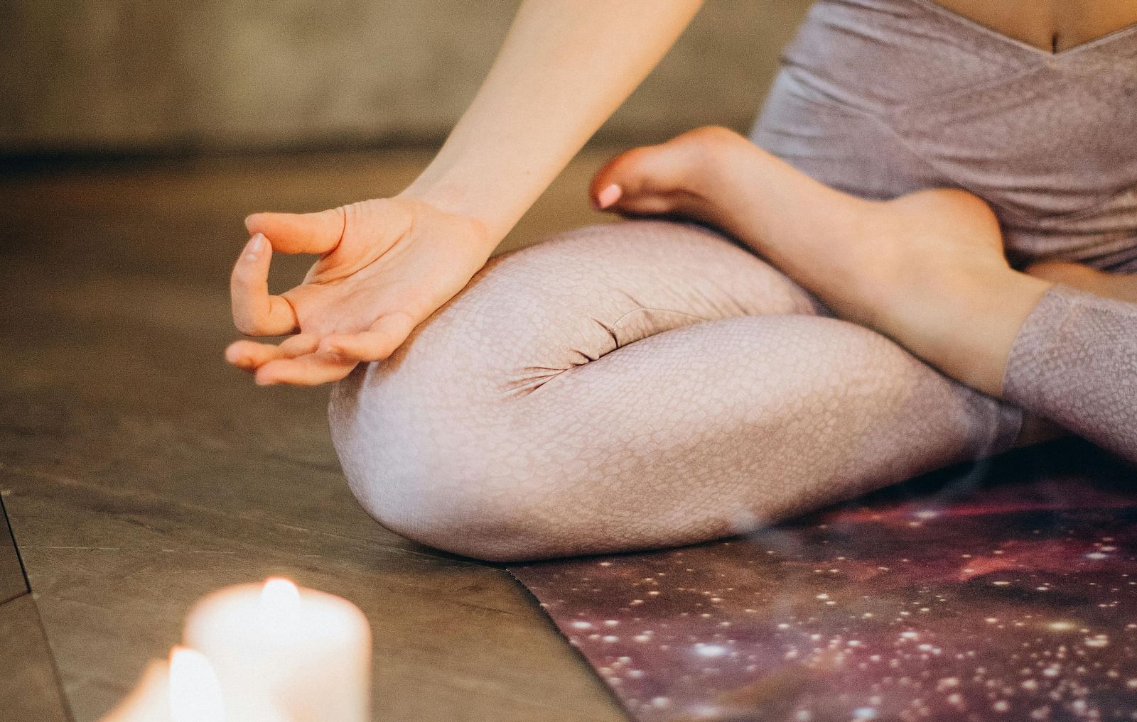 A woman on a prayer mat meditating while a candle is placed near her.