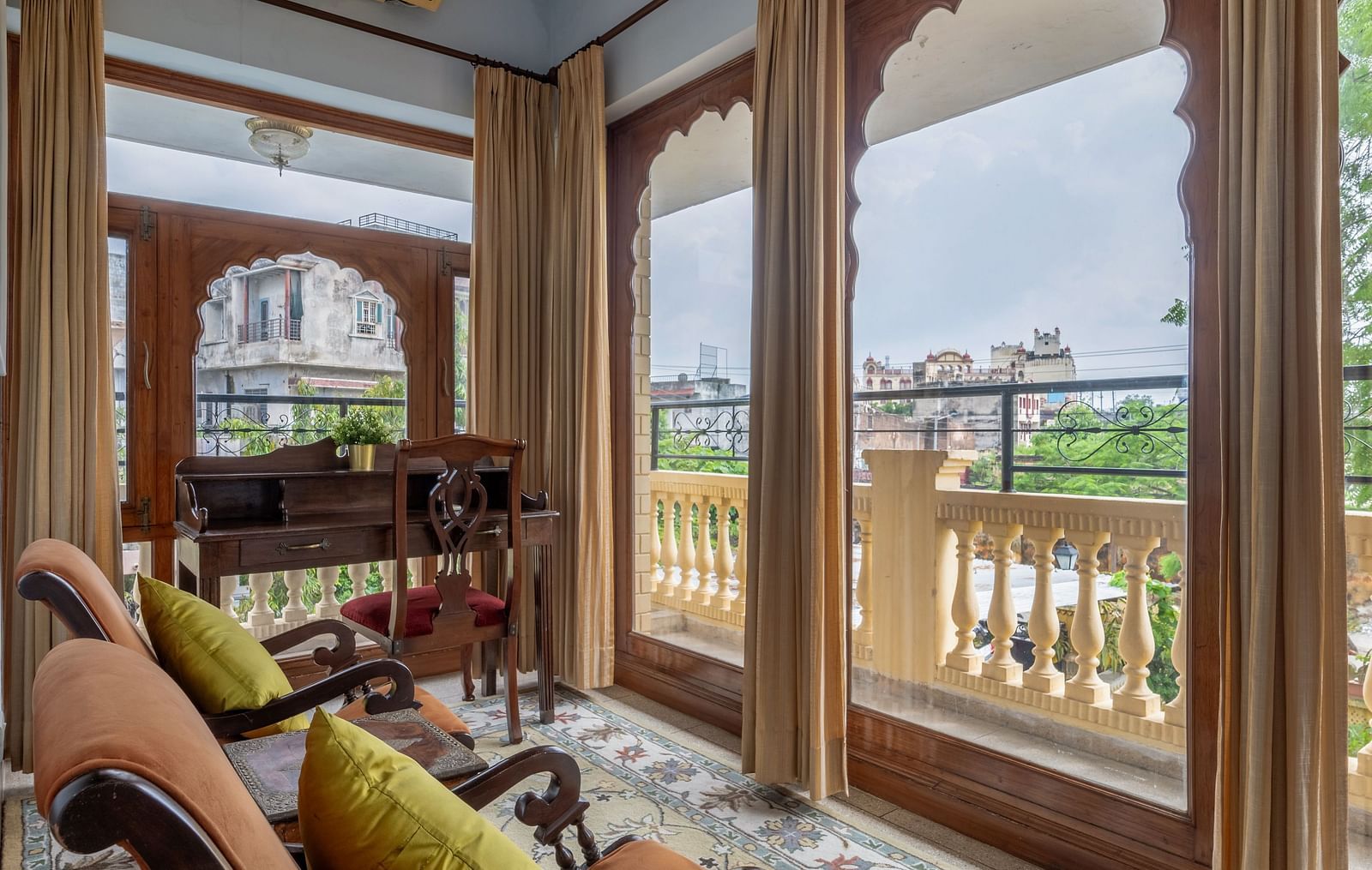A charming sitting area at Dera Rawatsar, Jaipur, offers comfortable chairs, arched doorways with scenic views, and a patterned rug on the floor.