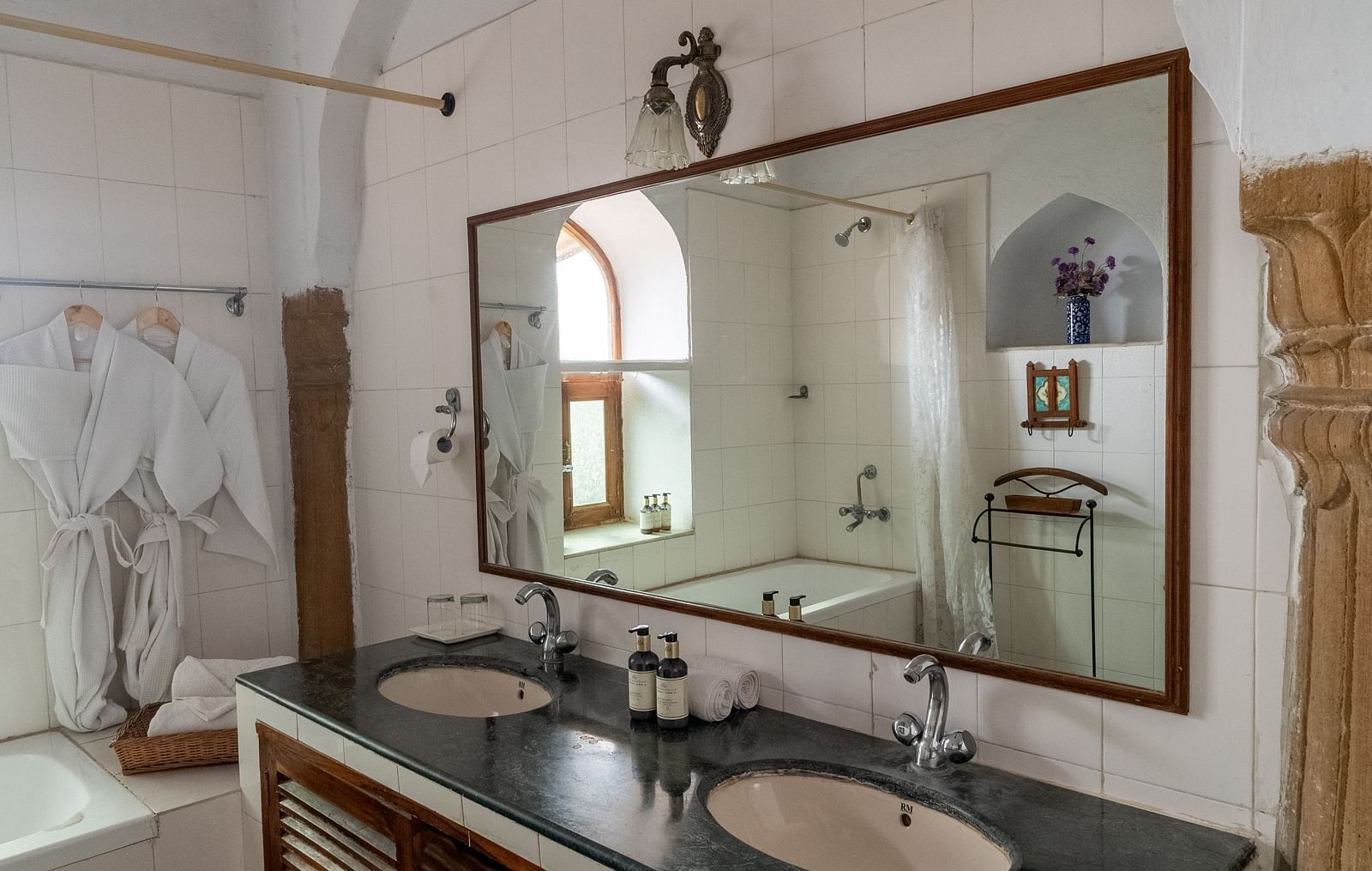 A bathroom at Fort Barli, Ajmer, has double sinks, a large mirror, and a glimpse of a bathing area.