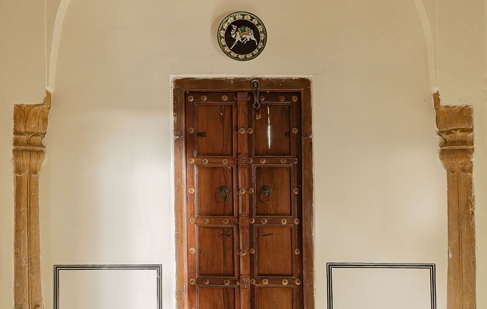 A carved wooden door stands under an arched opening at Fort Barli, Ajmer, flanked by decorative pillars.