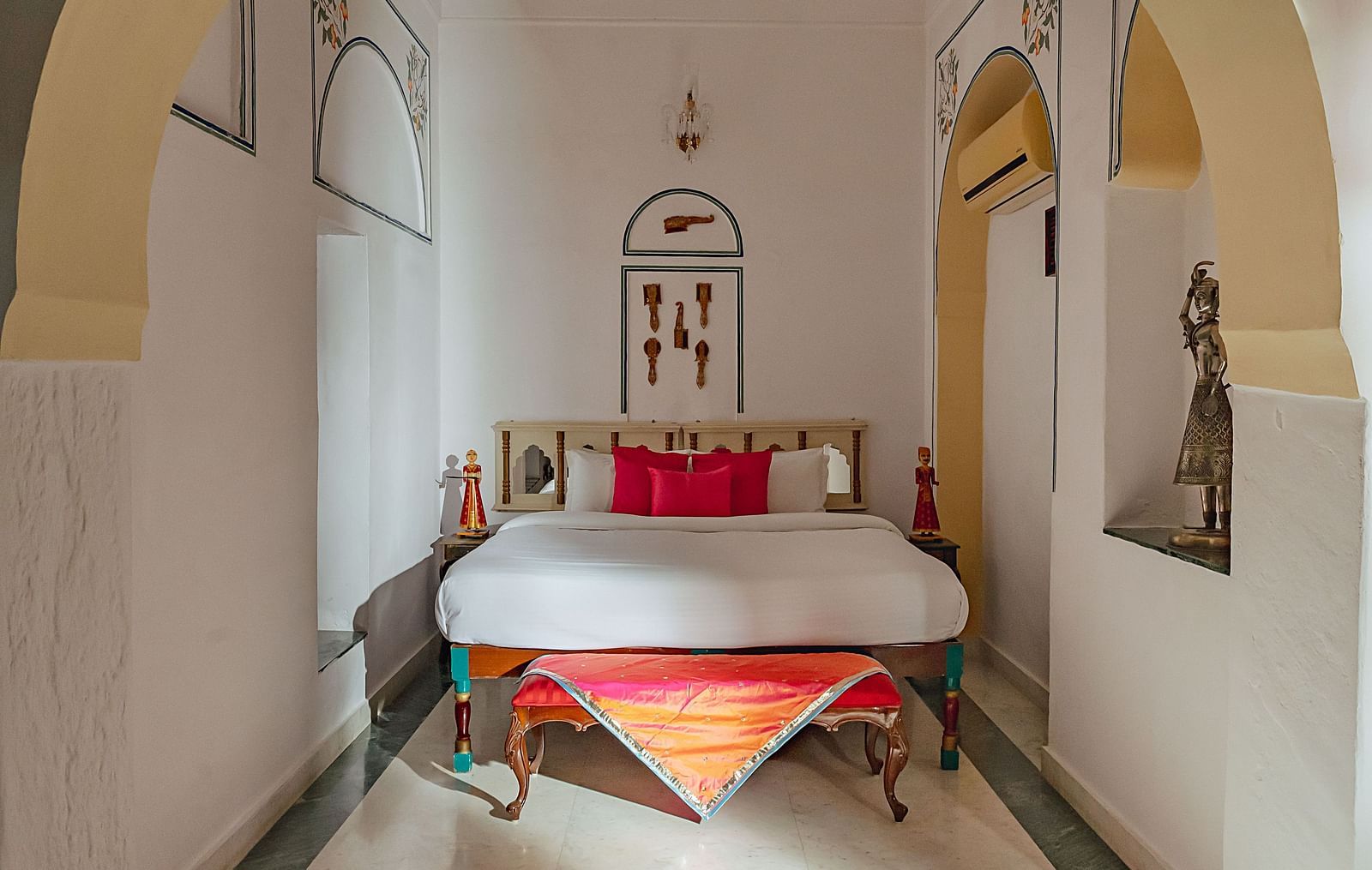 An arched passageway at Fort Barli, Ajmer, leads to a bed with colorful accents. Wall niches are visible.