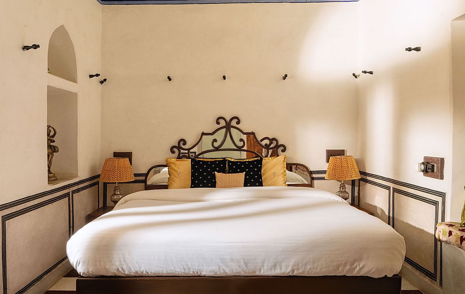 A bed with an elaborate headboard and footboard is centered in a room with a checkered floor at Fort Barli, Ajmer.