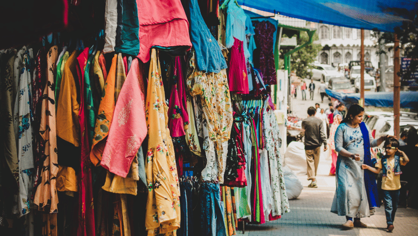 Colourful clothing stalls lining the busy shopping lanes of a market.