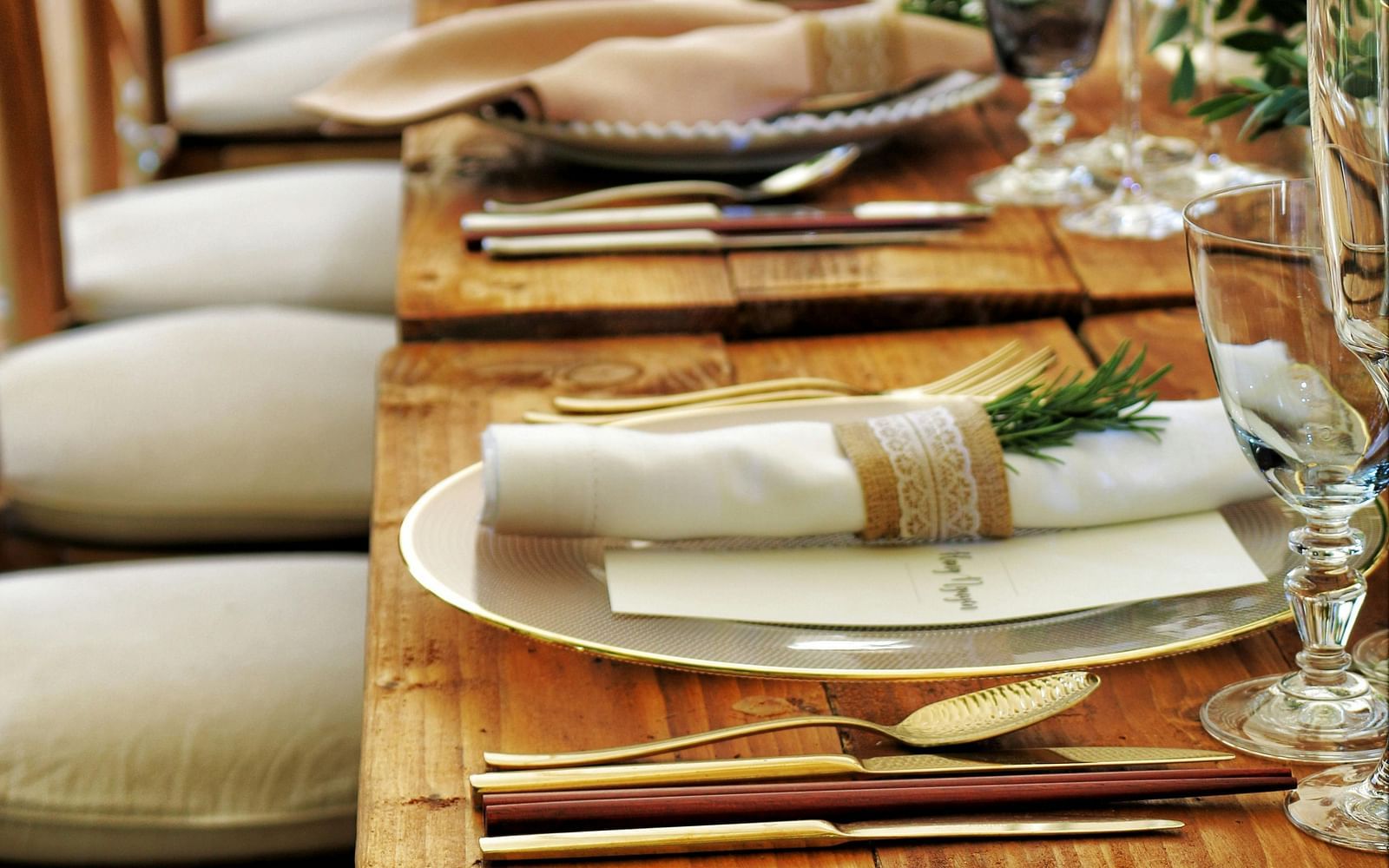 A long wooden table with beautifully set cutlery with small fern leaves in vases.