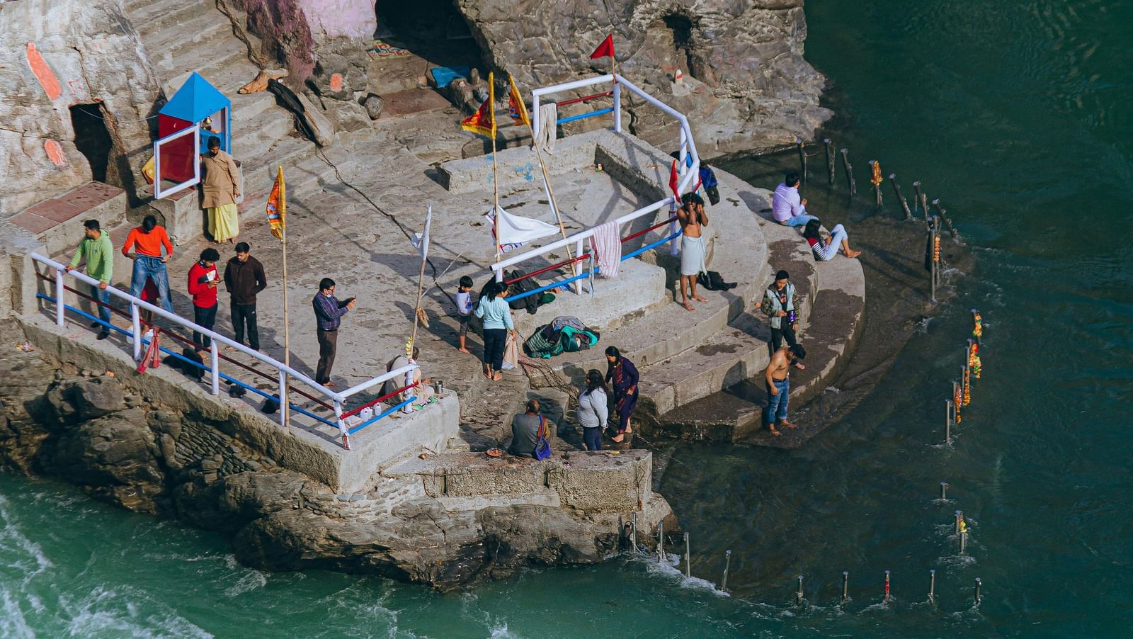 A high-angle view of a stone pier near a river, with devotees performing ritual.