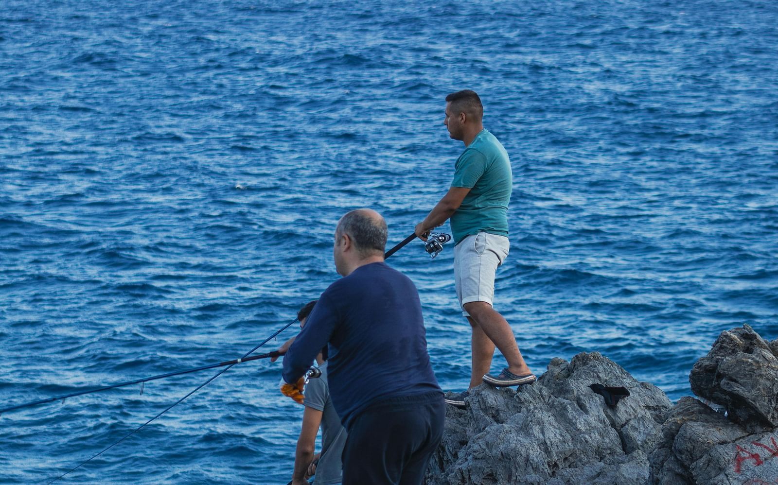 Two people standing on rocky cliffs overlooking a vast expanse of blue ocean.