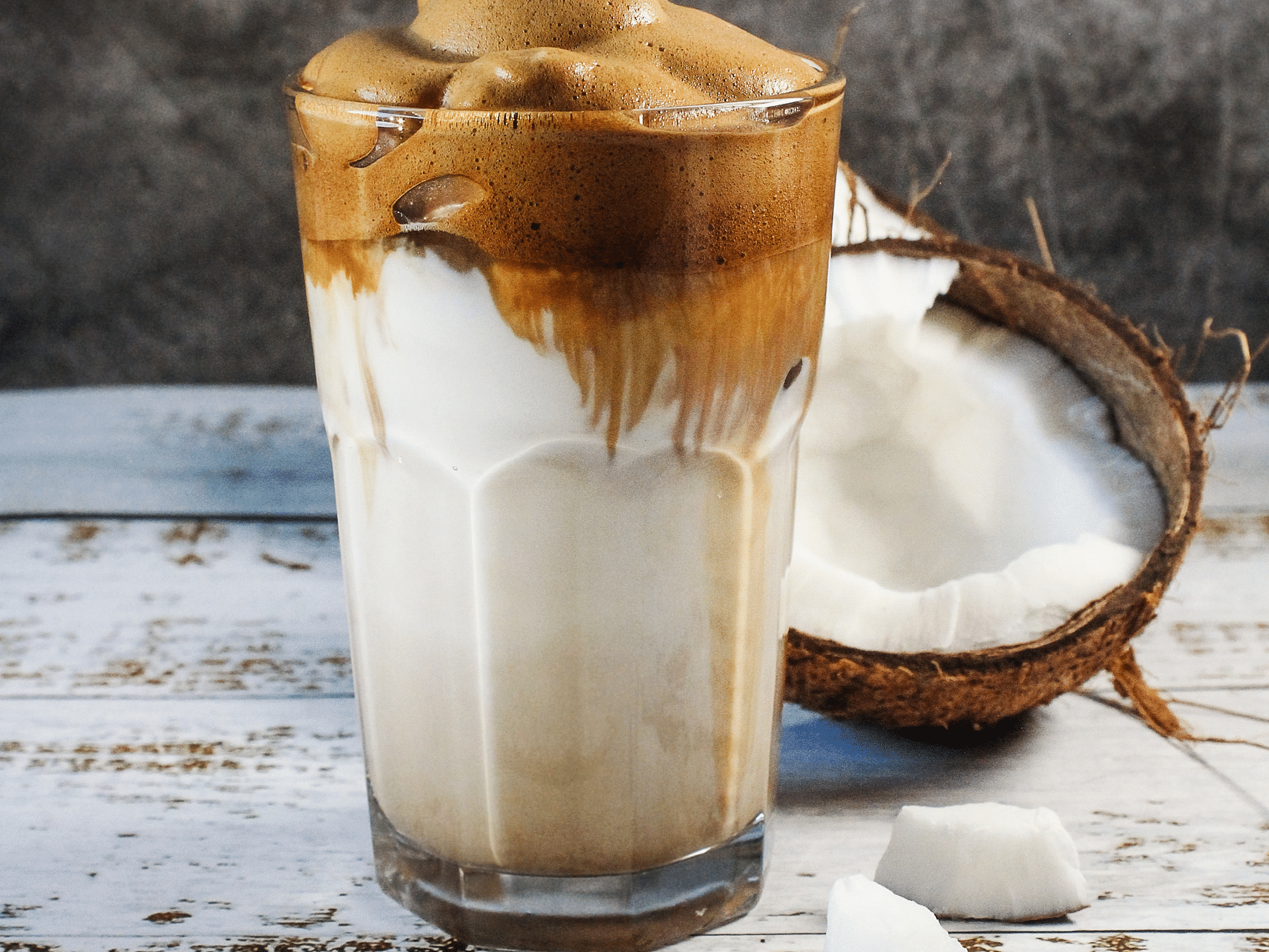 A coconut beverage with a cracked coconut beside it and coconut pieces nearby