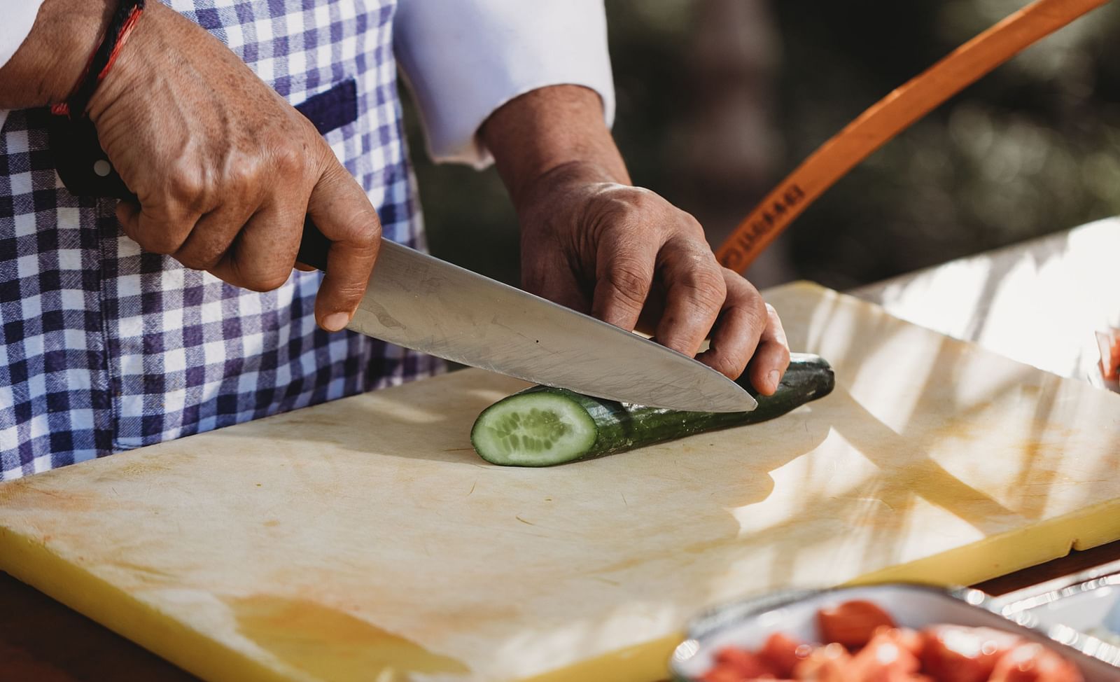 A person wearing a checkered apron is slicing a lime on a cutting board, with bowls of ingredients nearby, suggesting food preparation in an outdoor setting- Shahpura Bagh.