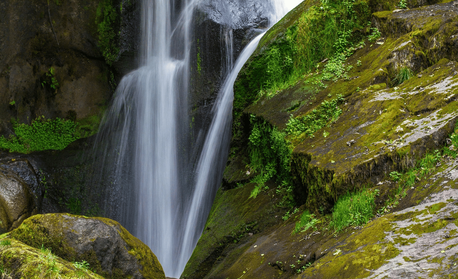 A long-exposure shot of a waterfall cascading down a moss-covered rock face in a lush forest.