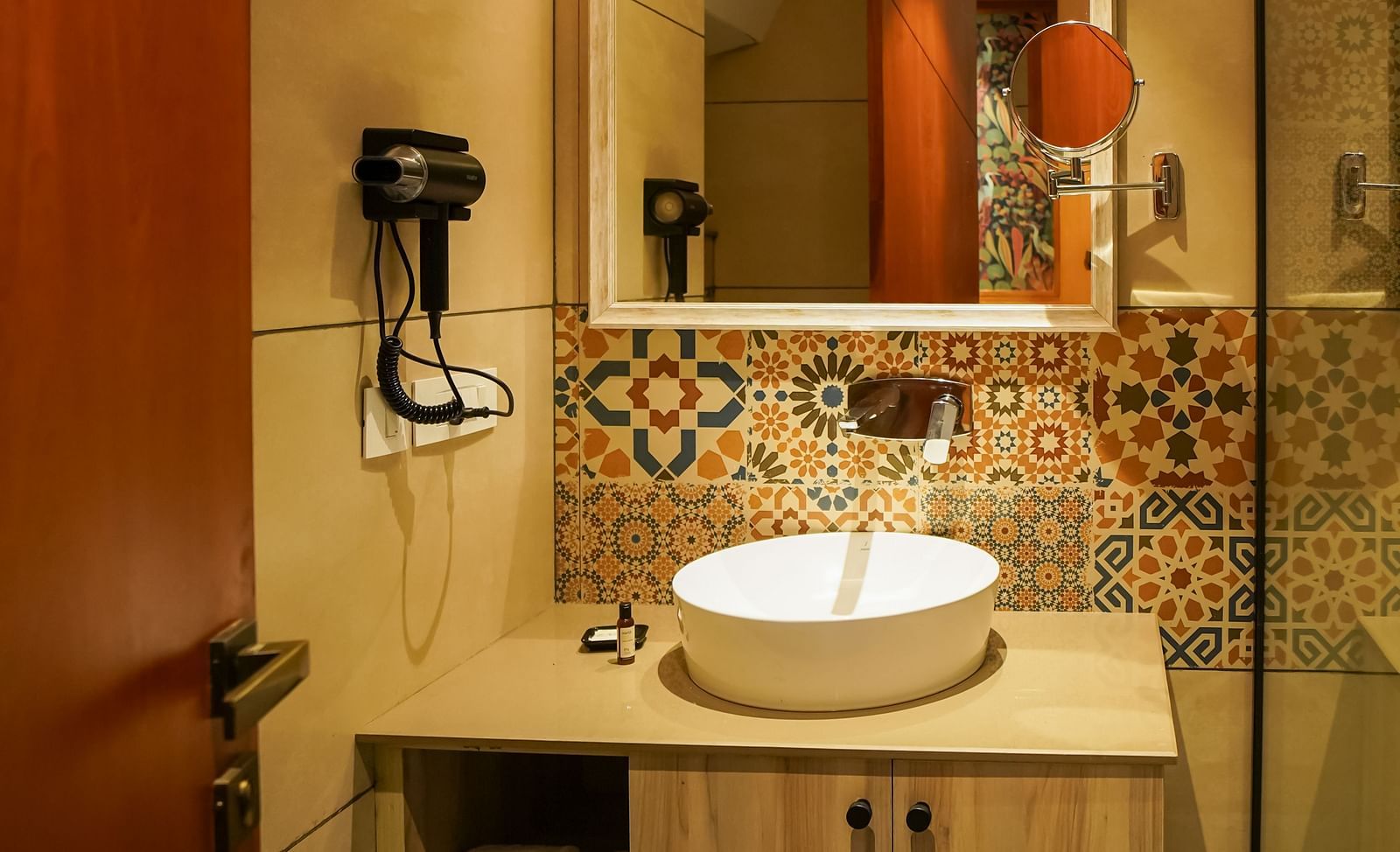 A modern bathroom features a vanity with a round basin sink, a large mirror, and a wall-mounted faucet, set against light-coloured walls | Deluxe Room with Valley View | Sukama Resort & Spa, Nainital