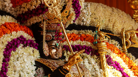 Idol of deity Murugan richly adorned with flower garlands, jewellery and ceremonial decorations inside a beautifully decorated temple shrine