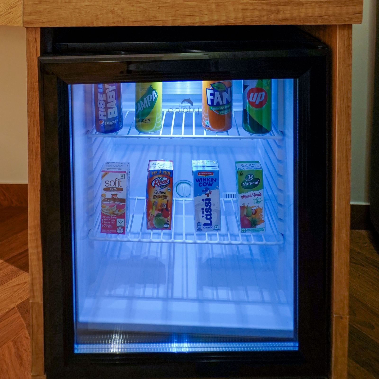 A small refrigerator with a glass door displays various beverages inside, topped by a tray holding mugs and a kettle - Hotel Park Inn, Nellore.