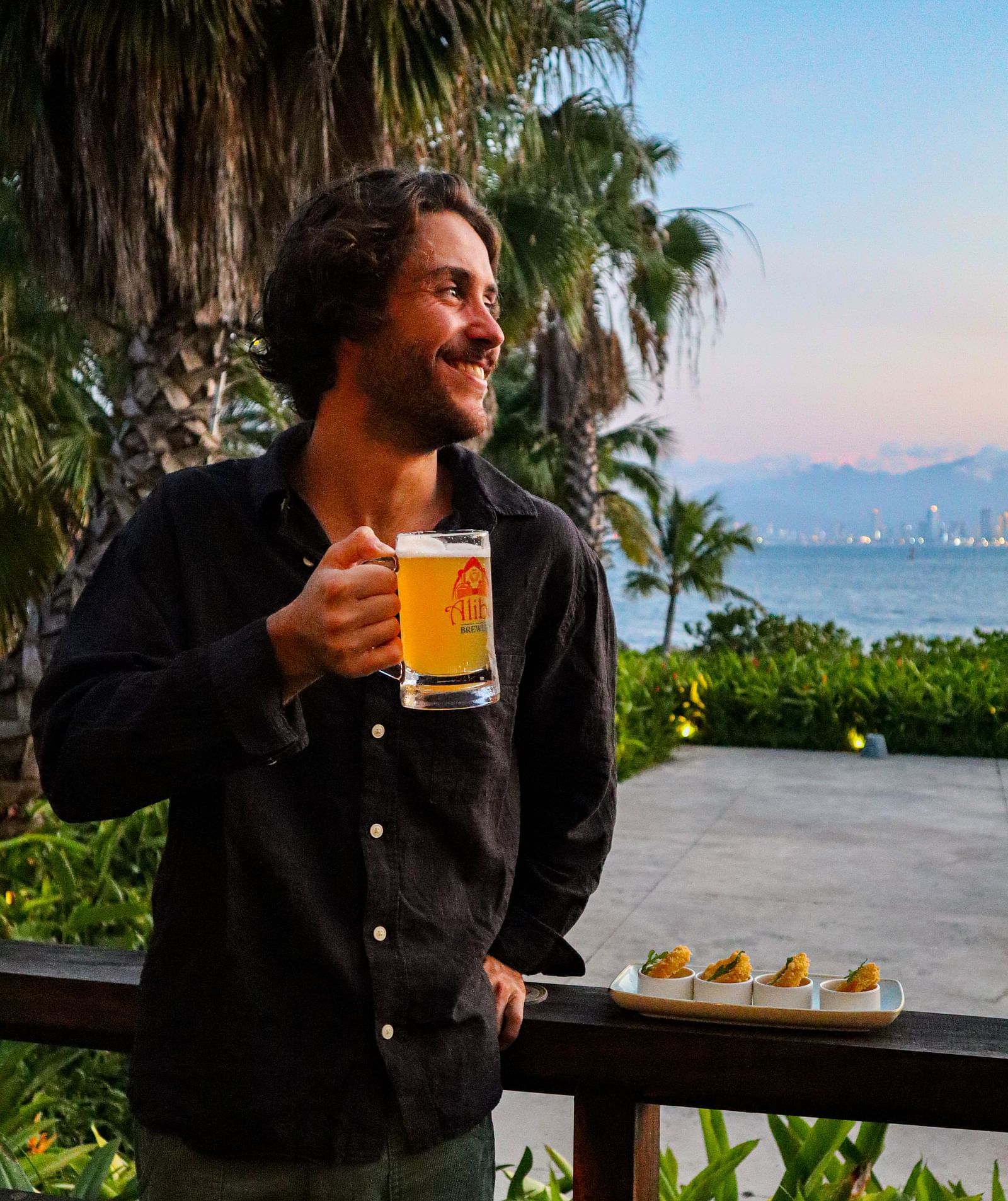 A person enjoying a beer pint with a serene sunset in the background - Alibu Resort Nha Trang
