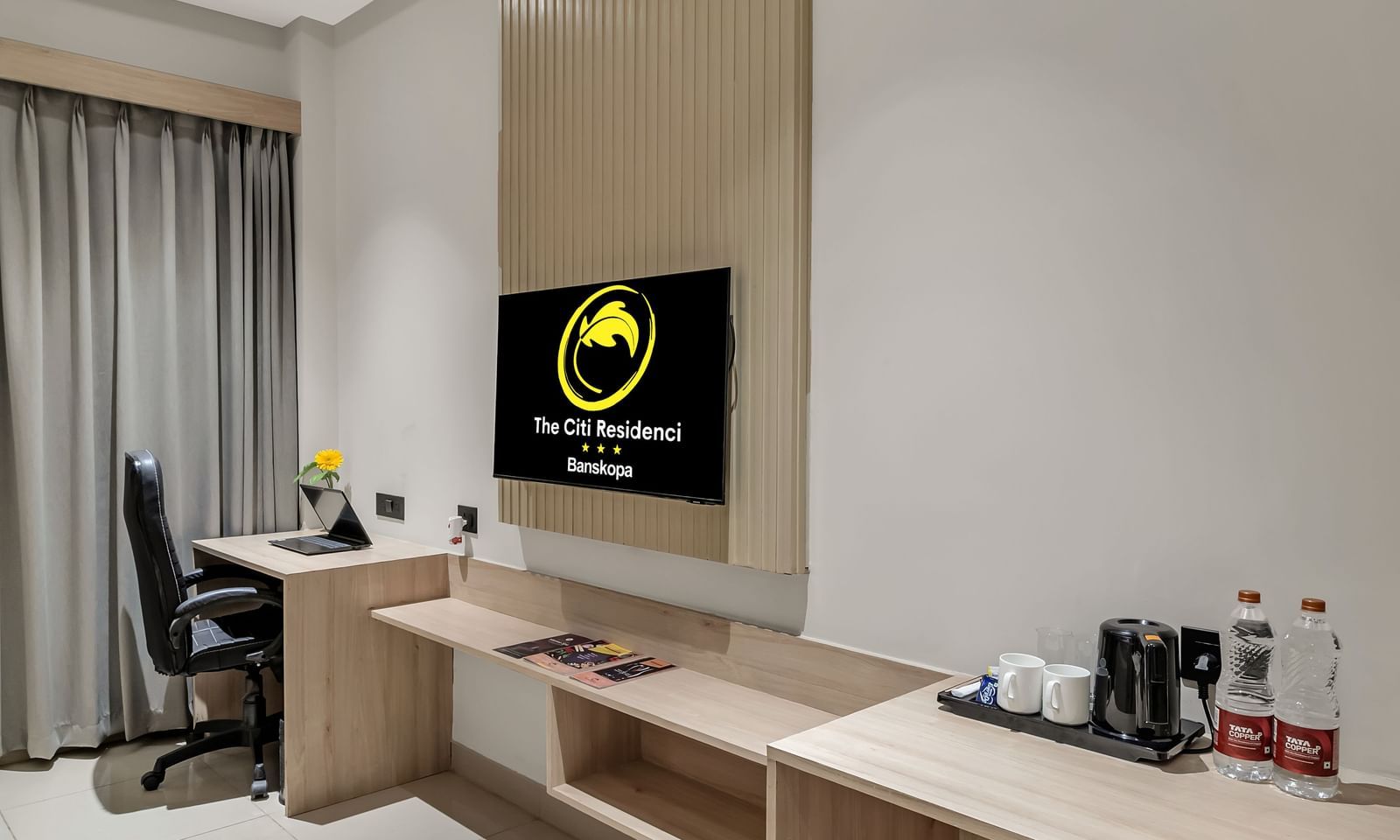 A modern hotel room featuring a work desk with a chair, a wall-mounted television, and a storage unit along a light-coloured wall | The Citi Residenci Hotel Banskopa