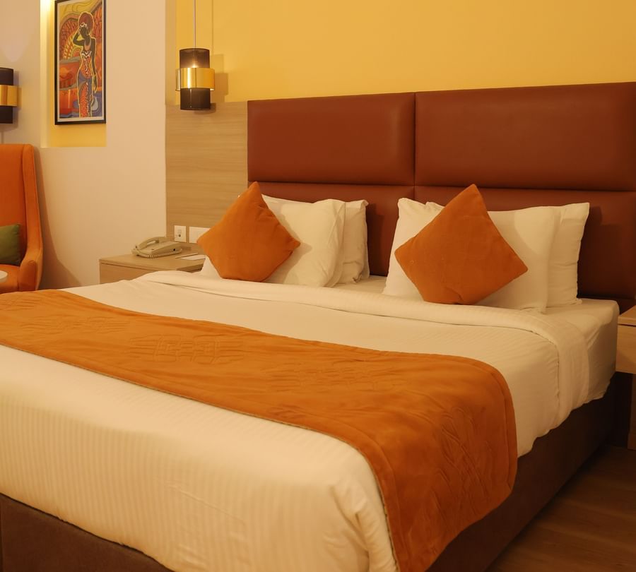 Hotel bedroom with orange pillows, white bedding, wooden headboard and bedside lamp at Best Western, Vrindavan.