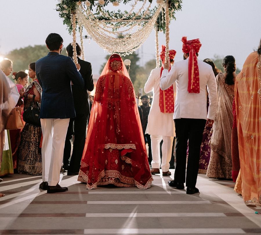 Bride walking down the aisle under floral arch at outdoor wedding mandap.