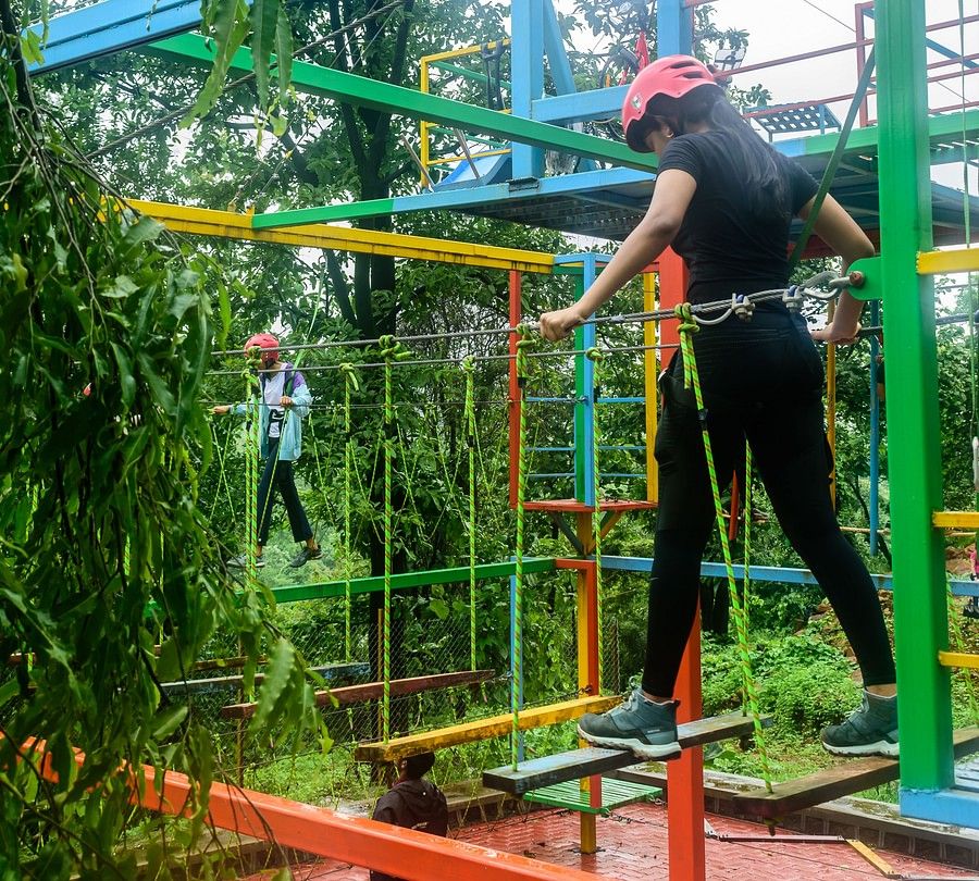 alt-text A portrait of a girl on a burma bridge with helmets and safety equipments making her way across the walkpath
