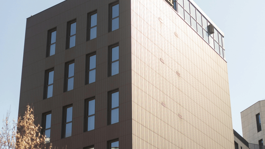 A tall rectangular building with rows of windows stands against a clear sky.
