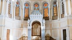 Interior of Paradesi Synagogue in Kochi with wooden benches, ornate ark with Star of David curtain, and stained glass windows above.
