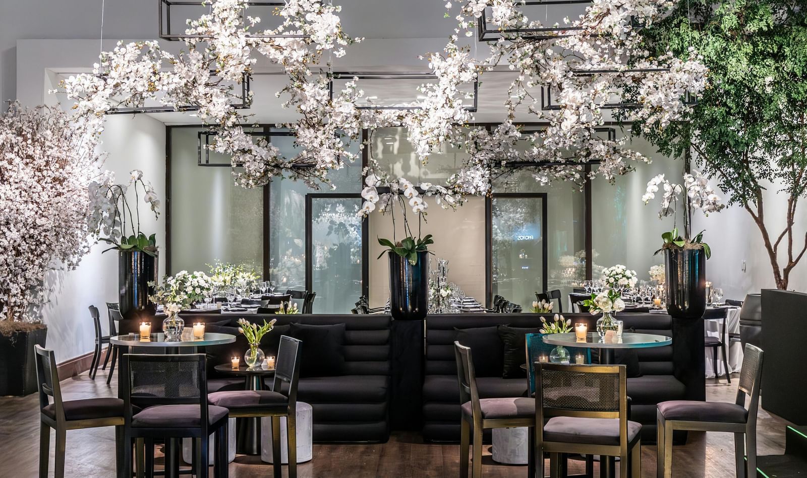 Brightly lit indoor event space with small tables, chairs, and floral decorations.