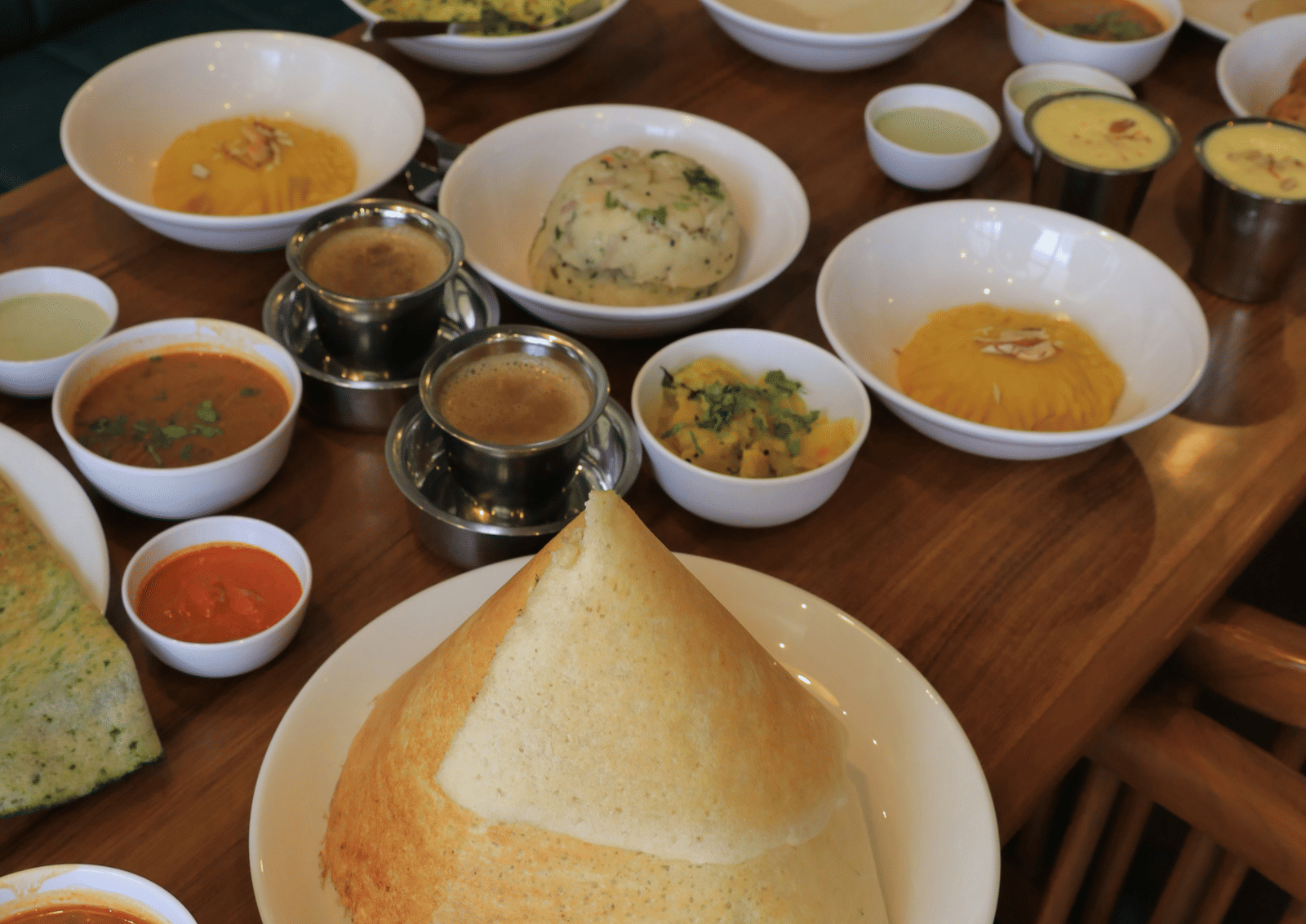A traditional South Indian meal served on a wooden table with various curries, chutneys, sambar, and crispy dosa - Zibe Coimbatore by GRT Hotels