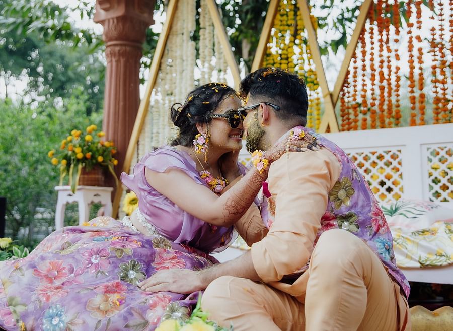 Bride and groom seated under a floral canopy, sharing an affectionate moment during a traditional ceremony.