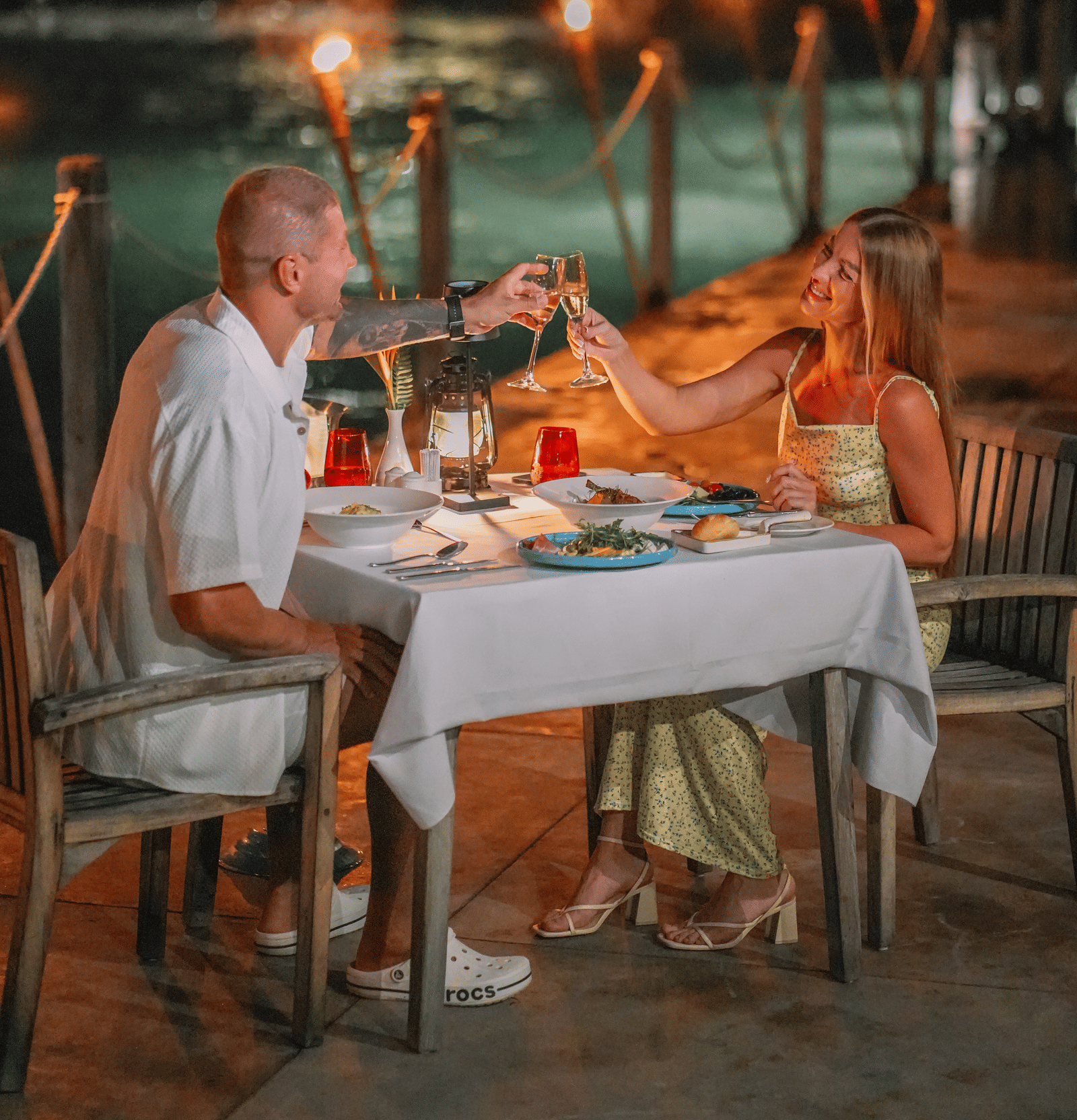 A couple in celebrating their Honey moon in Alibu Resort, Vietnam where two people are bringing their glasses together to celebrate near the beach.