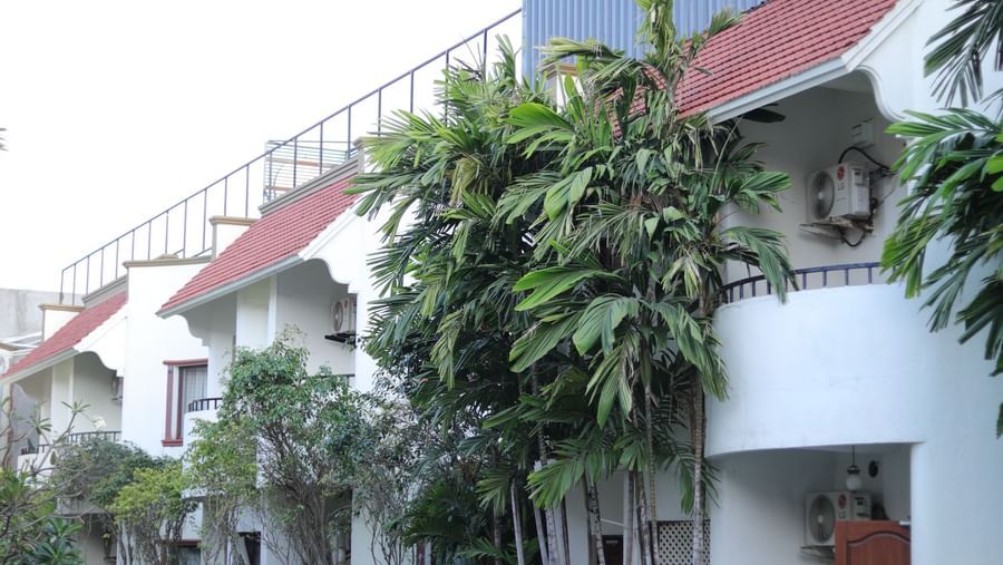 A partial, architectural shot of the hotel building exterior with a glimpse of the blue swimming pool and surrounding greenery at Ilara Hotels & Spa, OMR, Chennai.