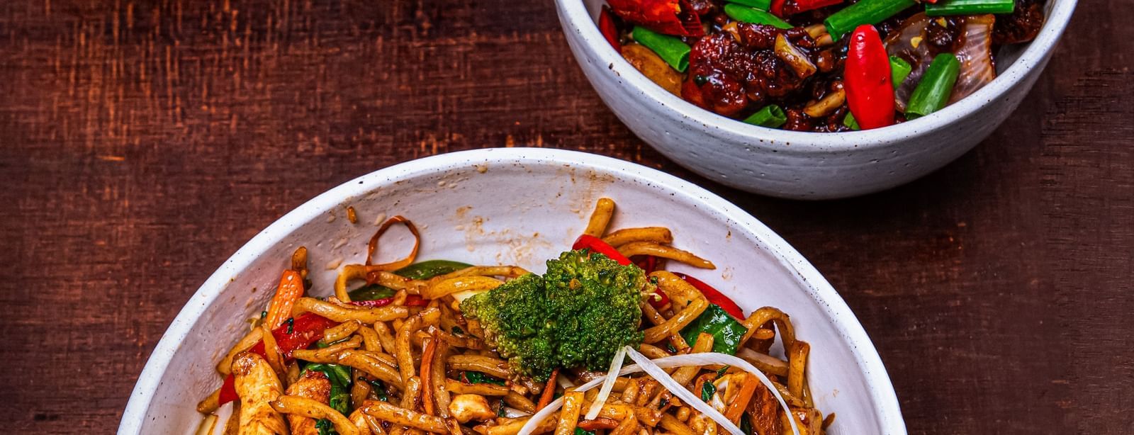 A white bowl filled with noodles topped with sprouts and herbs, served with a side of colorful vegetables in a separate bowl, placed on a dark wooden surface at The Hamuse Hotel, Kodaikanal.