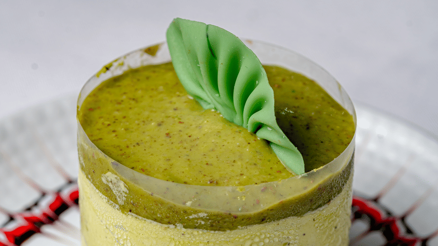 A pistachio mousse cake topped with a green leaf garnish at Café Latte, part of the Noor-Us-Sabah Palace, Bhopal, presented on a patterned dessert plate.