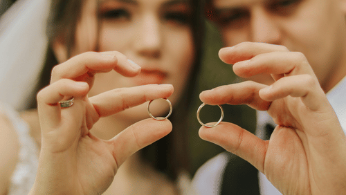 Image of newlyweds holding up wedding rings