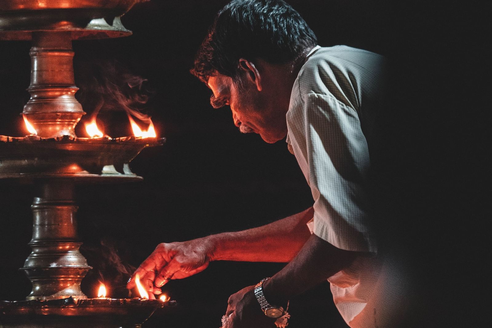 A man is lighting a tall lamp with numerous wicks placed in a circular manner