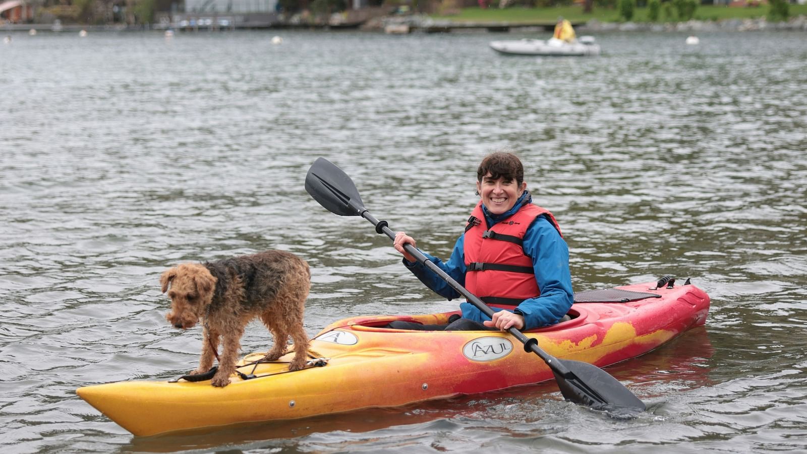 A solitary person kayaking with a dog on the kayak in a waterbody as seen from afar